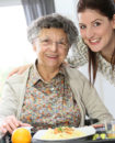 caregiver serving meal to elderly woman